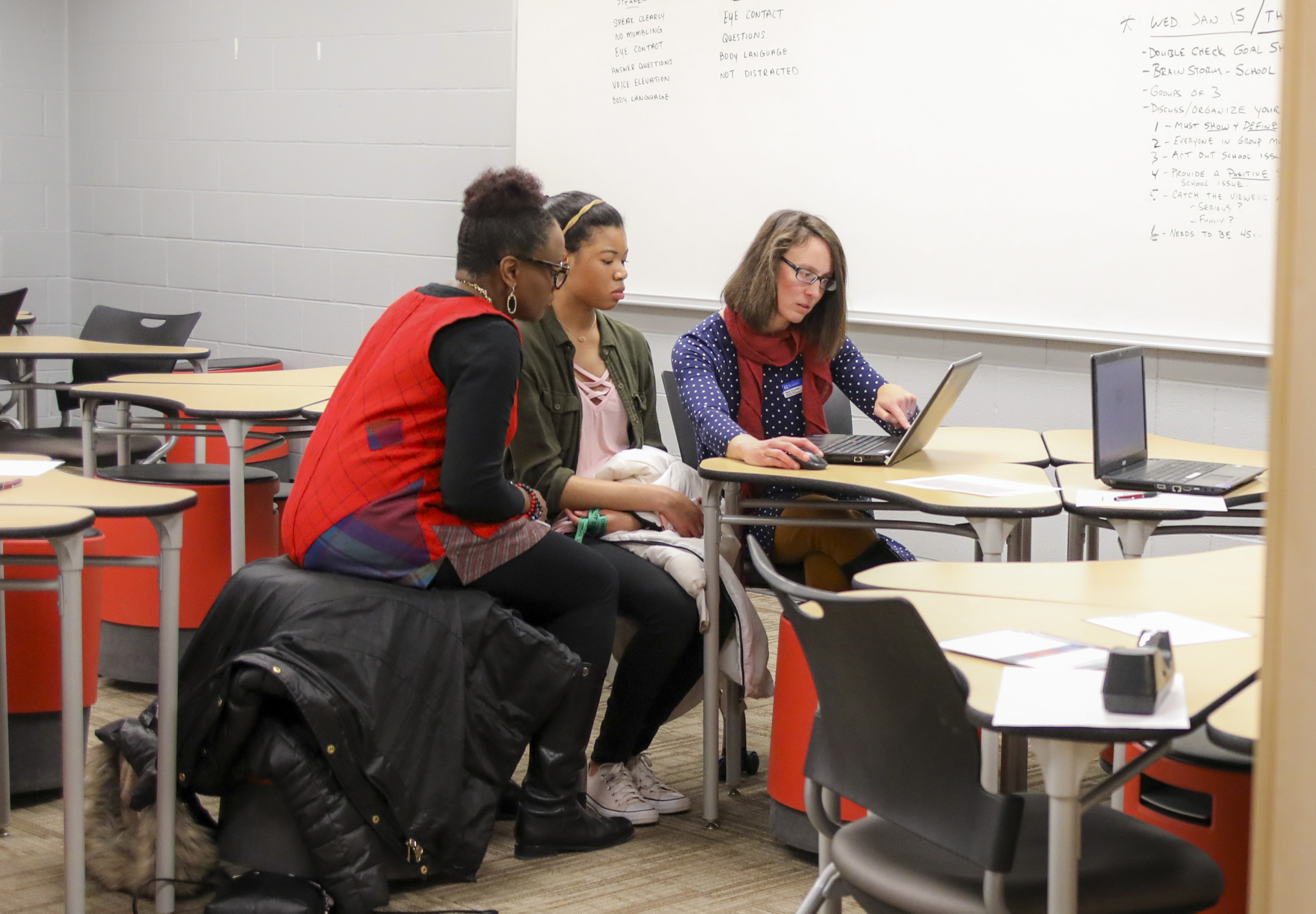 A TRIO advisor points at a computer showing something to a student and a parent